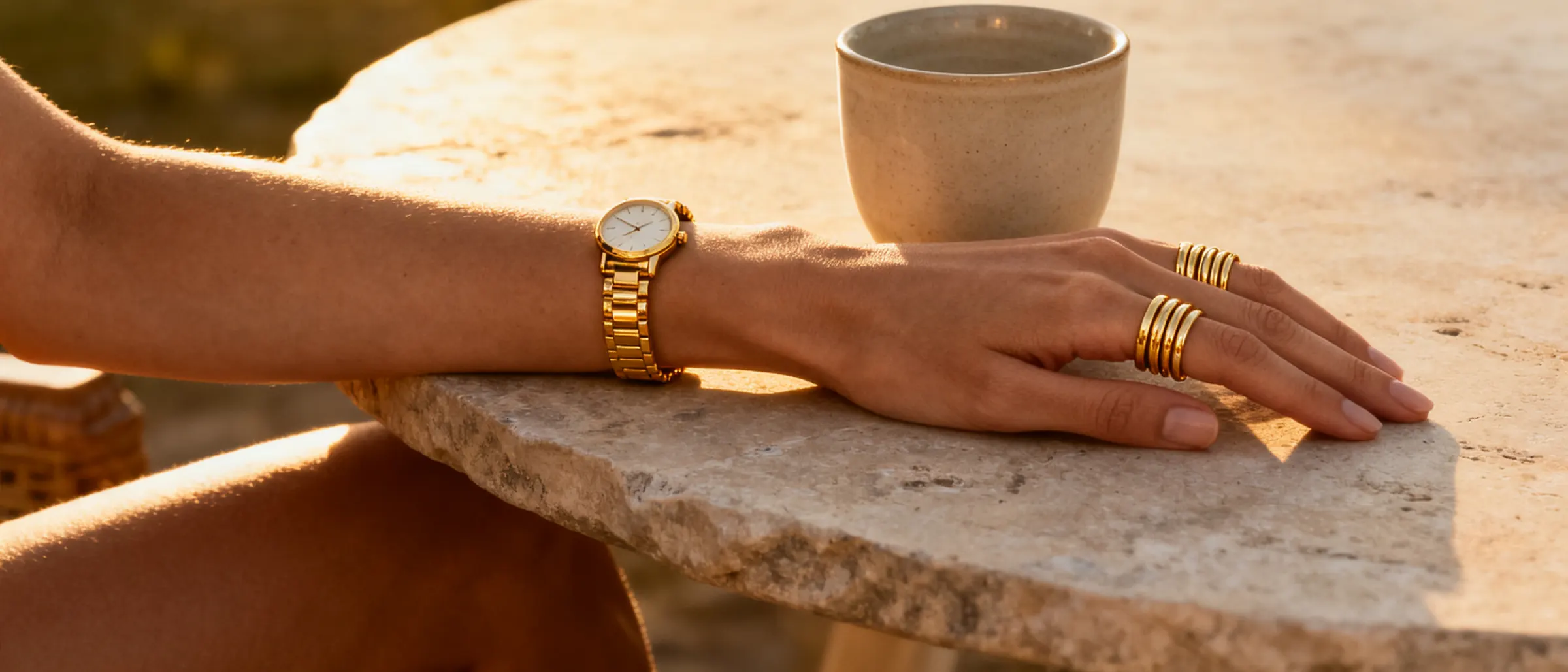 A wrist with a slim watch and stacked bracelets resting on travertine