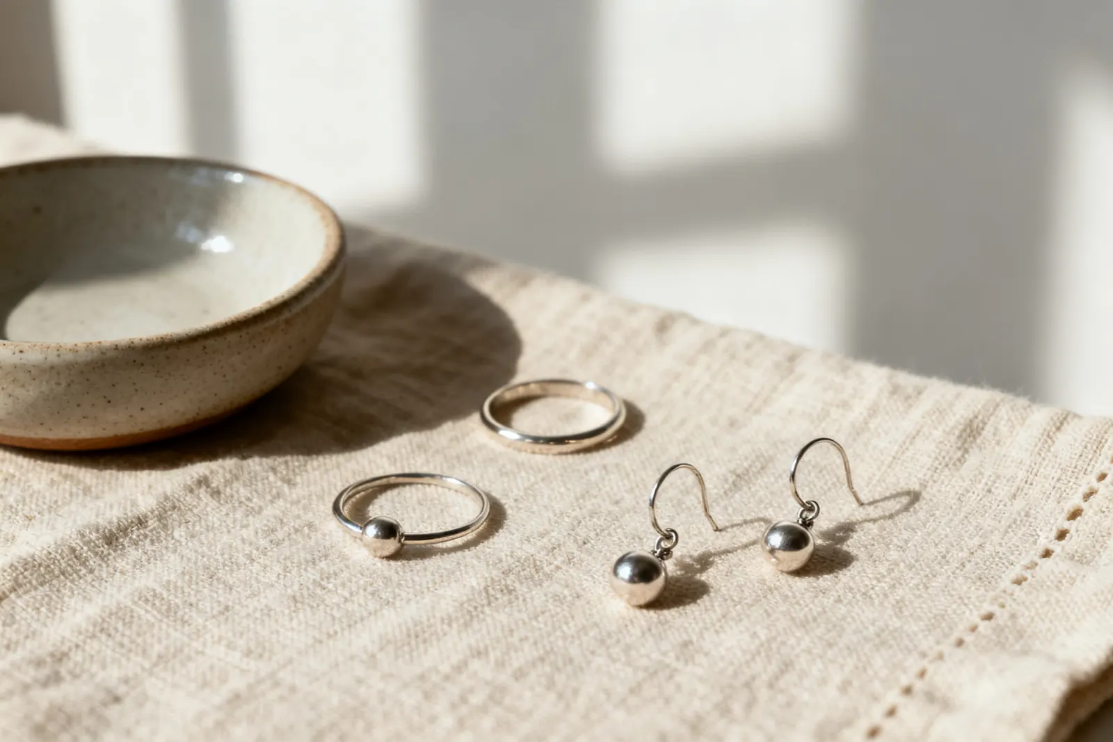 Rings and earrings laid out on a linen cloth beside a ceramic dish